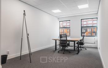 Kantoorruimte huren in Amsterdam Zuid-Oost met twee bureaus en stoelen, gelegen aan de Paasheuvelweg 20. Het kantoor biedt uitzicht op een moderne gevel en heeft een rustige sfeer.