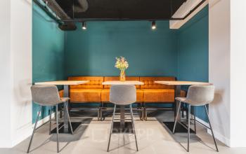 Kantoorruimte te huur in Amsterdam Zuid-Oost met een zithoek voorzien van moderne tafels, stoelen en een oranje bank tegen een turquoise muur op Paasheuvelweg 20.