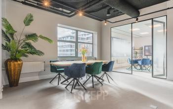 Moderne kantoorruimte in Amsterdam Zuid-Oost op Paasheuvelweg 20, met veel natuurlijk licht, glazen wanden en stijlvolle stoelen rondom een vergadertafel. Planten voegen een frisse touch toe.