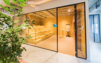 Moderne kantoorlounge met glazen wand, industrieel plafond en zitgedeelte, ideaal voor kantoorruimte huren in Amsterdam Zuid-Oost.