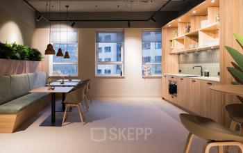 Moderne kantoorruimte huren in Amsterdam Zuid-Oost met strakke keuken, houten accenten en zitgelegenheid. Ideaal voor werk- en ontmoetingsmomenten in een aangename sfeer.