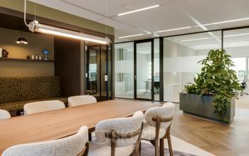 Moderne kantoorruimte op Herikerbergweg 290, Amsterdam Zuid-Oost, met houten tafel en comfortabele stoelen, ruime indeling, glazen wanden en groene planten. Ideaal voor kantoorruimte huren.