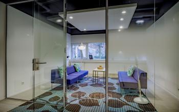 Modern kantoorpand op Hogehilweg 8 in Amsterdam Zuid-Oost met glazen wanden, kleurrijk tapijt en zithoek met bankstellen.