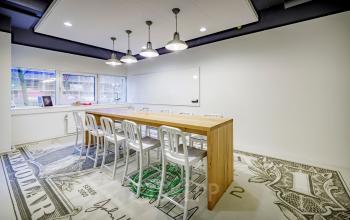 Vergaderruimte bij kantoor gelegen op Hogehilweg 8, Amsterdam Zuid-Oost, met houten tafel, metalen stoelen, grote raampartijen en opvallende vloerbedekking met geldprint.
