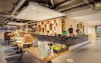 Kantoorruimte huren in Amsterdam Zuid-Oost, Karspeldreef 8. Moderne kantine met personeelslid achter de balie en ruime zitgelegenheid.