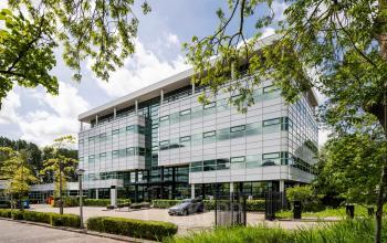 Modern kantoorpand gelegen aan de Burgemeester Stramanweg 102 in Amsterdam Zuid-Oost, omgeven door groen met grote ramen die veel licht binnenlaten.