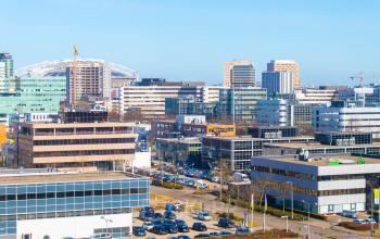 Uitzicht op kantoorpanden aan de Laarderhoogtweg 25 in Amsterdam Zuid-Oost. Diverse gebouwen en parkeerplaatsen zijn zichtbaar onder een heldere blauwe hemel.