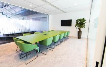 Moderne vergaderruimte in Amsterdam Zuid-Oost met lange groene tafel en twaalf stoelen. Het kantoorpand Laarderhoogtweg 25 biedt ruimte voor zakelijke bijeenkomsten in een lichte omgeving.