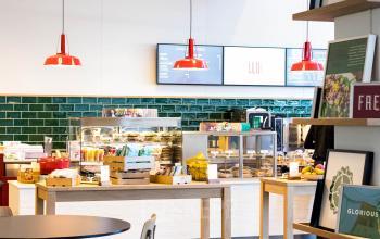 Een moderne kantoorruimte in Amsterdam Zuid-Oost met een uitnodigende pantry voorzien van tafels, stoelen en rood accentverlichting, ideaal om te huren voor een aangename werkervaring.