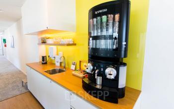 Gezellige pantry in kantoorpand Laarderhoogtweg 25, Amsterdam Zuid-Oost met koffieautomaat, frisgele muur en nette opbergkasten. Ideaal voor wie kantoorruimte wil huren.