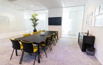 Moderne vergaderruimte in een kantoorpand op Laarderhoogtweg 25, Amsterdam Zuid-Oost met een lange tafel, gele stoelen, en een grote plant naast het scherm aan de muur.