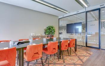 Een moderne vergaderruimte in een kantoorpand in Amsterdam Zuid-Oost, met een grote tafel, rode stoelen en een groot scherm. Een ideale plek voor zakelijke bijeenkomsten of kantoorruimte huren.