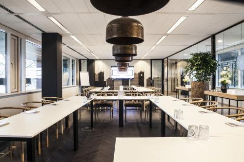 Moderne vergaderruimte met grote ramen en glazen scheidingswanden in kantoorpand aan De Entree 99-197, Amsterdam Zuid-Oost. Stoelen rondom tafels, plant in de hoek.