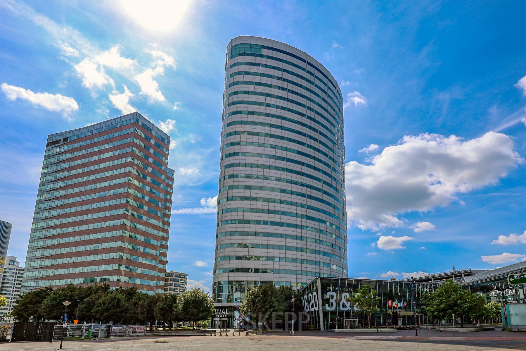 Modern kantoorpand op De Entree 99-197 in Amsterdam Zuid-Oost met indrukwekkende gevel en glaswerk. Ideaal voor kantoorruimte huren. Blauw lucht complimenteert het ontwerp van de moderne kantoren.