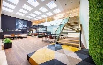 Kantoorruimte huren aan de Herikerbergweg 1-35 in Amsterdam Zuid-Oost met moderne inrichting, veel natuurlijk licht, een centrale trap en een groene wand.