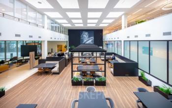 Moderne werkruimte in kantoor op Herikerbergweg 1-35, Amsterdam Zuid-Oost, met ruime opzet, houten vloeren en diverse comfortabele werkplekken. Mensen werkzaam aan bureaus.