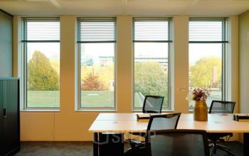 Kantoorruimte huren aan Jachthavenweg 109-A, Amsterdam Zuidas. Heldere ruimte met grote ramen, bureaus, stoelen en een kast, omgeven door een groen uitzicht.