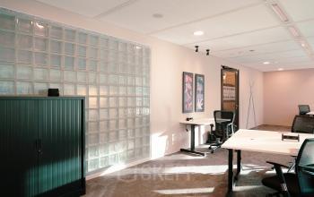 Kantoorruimte huren op Jachthavenweg 109-A in Amsterdam Zuidas. Modern interieur met bureaus, stoelen, kast en glazen wand.
