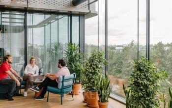 Kantoorruimte huren op Strawinskylaan 4117 in Amsterdam Zuidas, met drie mensen in een gesprek bij een raam met veel planten.