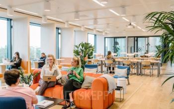 Kantoorruimte huren op Strawinskylaan 4117, Amsterdam Zuidas met moderne, lichte inrichting, grote ramen en gemeenschappelijke zitplaatsen. Medewerkers bezig met laptops en vergaderingen.