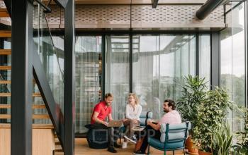 Moderne kantoorruimte huren aan de Strawinskylaan 4117, Amsterdam Zuidas, met comfortabele zitplekken en veel natuurlijk lichtinval. Drie mensen zijn in gesprek en gebruiken een laptop.