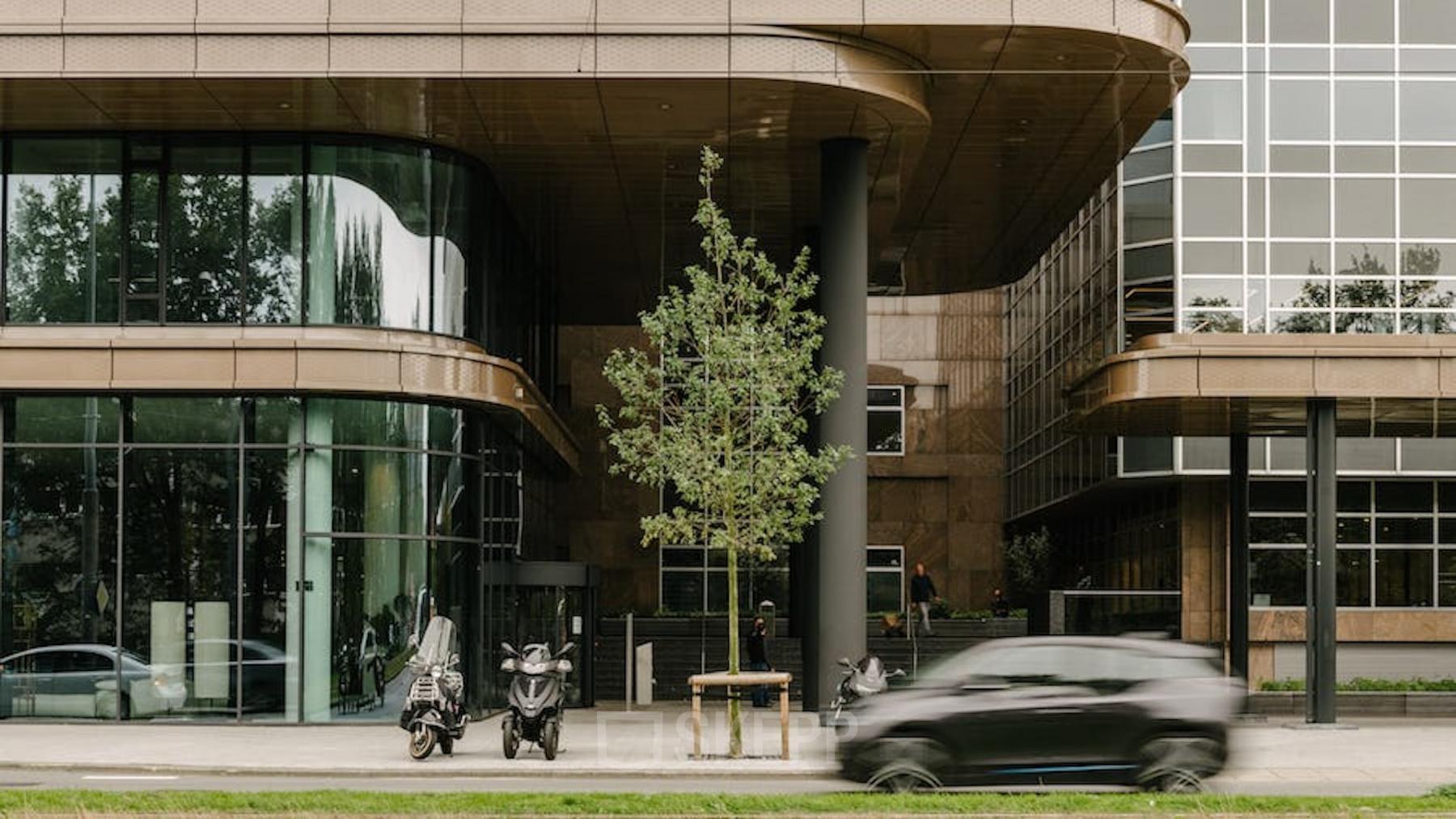 Modern kantoorpand op Strawinskylaan 4117, Amsterdam Zuidas. Voorgevel met glazen panelen en motoren geparkeerd aan de zijkant. Kantoorruimte huren in zakelijke omgeving.
