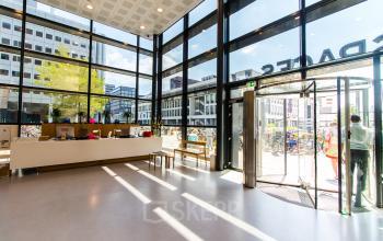 Lichte en open entree van een kantoorpand op Barbara Strozzilaan 101-201 in Amsterdam Zuidas, met glazen wanden, een balie en mensen die binnenkomen en vertrekken.