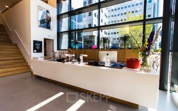 Lichte receptieruimte in een kantoorpand op Barbara Strozzilaan 101-201, Amsterdam Zuidas. Een medewerker zit achter de balie met open laptop en kantoorbenodigdheden.