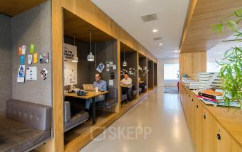 Moderne kantoorruimte op Barbara Strozzilaan 101-201 in Amsterdam Zuidas met werkruimtes en mensen die aan tafel laptops gebruiken. Ideaal voor bedrijven die een kantoorpand willen huren.