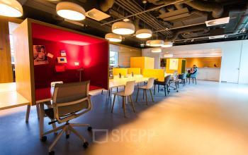 Moderne kantoorruimte in Amsterdam Zuidas met kleurrijke werkplekken en enkele mensen die samenwerken. Ideaal voor kantoorruimte huren met flexibele indeling en een inspirerende omgeving.