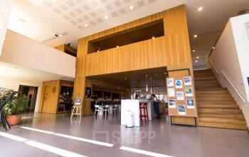 Moderne kantoorruimte op Barbara Strozzilaan 101-201 in Amsterdam Zuidas met houten elementen, een centrale trap en een gemeubileerde ontvangstgedeelte met balie en zitplaatsen. Ideaal om te huren voor jouw kantoor.