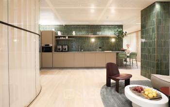 Kantoorruimte huren op Beethovenstraat 503, Amsterdam Zuidas, met gemeubileerd interieur, waaronder een zithoek en pantry waar iemand aan het werk is aan een tafel.