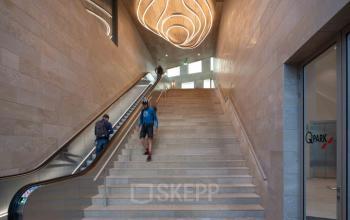 Ingang van modern kantoorpand aan de Beethovenstraat 503, Amsterdam Zuidas met indrukwekkende trap en unieke verlichting. Mensen lopen naar boven, ideaal als kantoorruimte huren in Amsterdam.