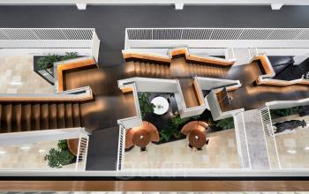 Moderne, ruimtelijke kantoorpand in Amsterdam Zuidas met strakke lijnen en uitnodigende houten trappen. Planten en tafels zichtbaar. Perfect voor kantoorruimte huren in een inspirerende omgeving.