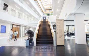 Moderne kantoorruimte met open vloerplan op Fred. Roeskestraat 115, Amsterdam Zuidas, met een centrale trap en mensen bezig met zakelijke activiteiten.