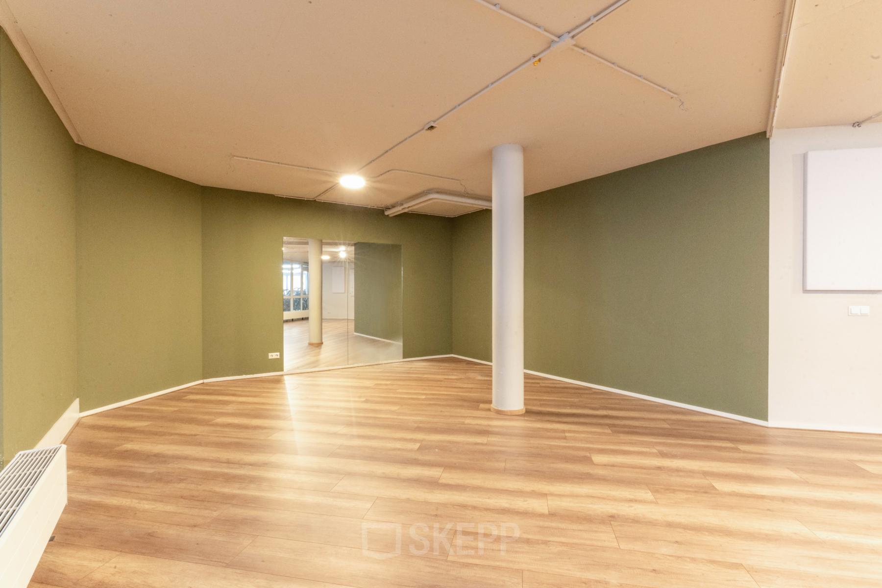 Leeg kantoorpand met houten vloer en groen geverfde muren op De Boelelaan 1110 in Amsterdam Zuidas, ideaal voor het huren van kantoorruimte.
