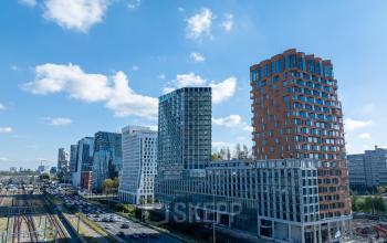 Moderne kantoorpanden langs de Hildegard Von Bingenstraat, Amsterdam Zuidas, met blauwe lucht en stadsverkeer.