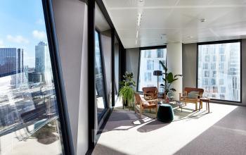 Mooie, lichte kantoorruimte te huur in Amsterdam Zuidas, met grote ramen en uitzicht op de stad. De ruimte is gemeubileerd met elegante stoelen en tafels, omringd door moderne architectuur.