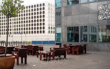 Exterieur van een kantoorpand aan de Barbara Strozzilaan 101, Amsterdam Zuidas, met houten zitplaatsen buiten. Ideaal voor wie kantoorruimte huren wil in een dynamisch omgeving.