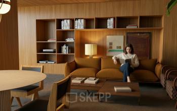 Stijlvolle kantoorruimte huren aan de Barbara Strozzilaan 101 101 in Amsterdam Zuidas met houten interieur en comfortabele zitmogelijkheden, waar een persoon rustig met een boek bezig is.