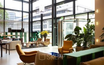 Moderne werkruimte in kantoorpand op Barbara Strozzilaan 101, Amsterdam Zuidas, met comfortabele zitplekken, veel groen en grote ramen voor natuurlijk licht.