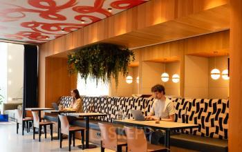 Stijlvolle kantoorruimte op Barbara Strozzilaan 101, Amsterdam Zuidas, met moderne houten afwerking, kleurrijke plafondkunst en comfortabele zitgelegenheden. Personen zijn bezig met laptops. Geschikt voor kantoorruimte huren.