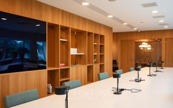 Moderne kantoorruimte met lange witte tafel, stoelen en ingebouwde kasten, ideaal voor vergaderingen of samenwerking. Perfect voor bedrijven die kantoorruimte willen huren in Amsterdam Zuidas.