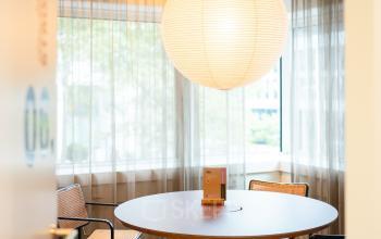 Gezellige kantoorruimte huren op Barbara Strozzilaan 101 in Amsterdam Zuidas, met een ronde tafel en moderne stoelen onder een grote, hangende lamp.