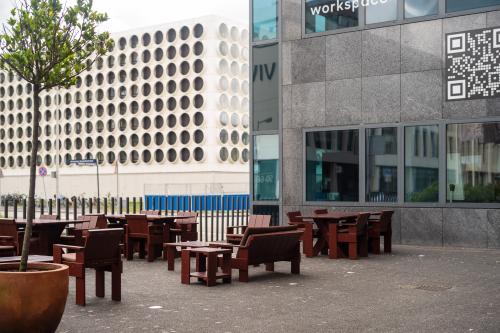 Exterieur van een kantoorpand aan de Barbara Strozzilaan 101, Amsterdam Zuidas, met houten zitplaatsen buiten. Ideaal voor wie kantoorruimte huren wil in een dynamisch omgeving.