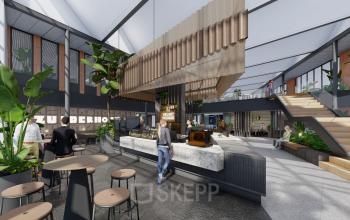 Moderne kantoorruimte in Amsterdam Zuidas met een open vloerplan, voorzien van een centraal koffiepunt en diverse werkplekken. Mensen werken en converseren in een lichte, groene omgeving.