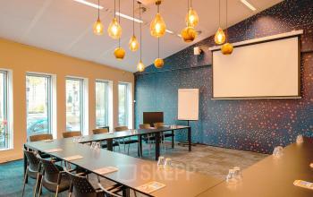 Vergaderruimte te huur in Amsterdam Zuidas met lange tafels, stoelen en modern verlichtingsontwerp, gelegen op Jachthavenweg 109, ideaal voor kantoorbijeenkomsten.