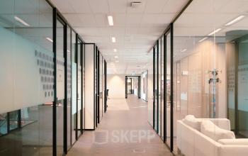 Lichte, moderne gang in een kantoorpand aan de Jachthavenweg 109, Amsterdam Zuidas. Glazen wanden geven toegang tot verschillende kantoren. Ideale plek voor kantoorruimte huren.