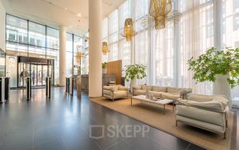Moderne entree van kantoorpand op Claude Debussylaan 10, Amsterdam Zuidas, met stijlvolle zitplekken, hoge ramen en veel lichtinval.