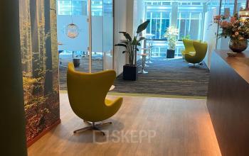 Ingang van het kantoorpand op Claude Debussylaan 10, Amsterdam Zuidas; moderne lobby met houten vloer, gele stoelen en decoratieve accenten.